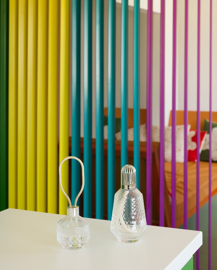 Detalle encimera de cocina blanca con embases de cristal tallado y al fondo los listones metálicos de colores