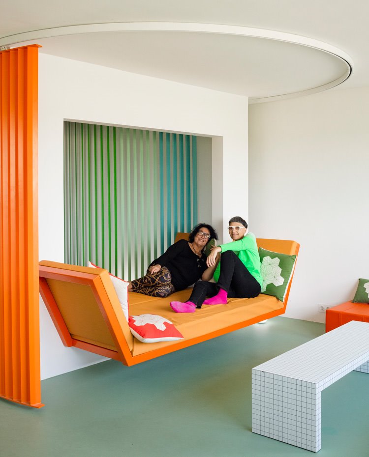 Matalí Crasset y acompañante sobre sofá-cama naranja, con biombo circular multicolor