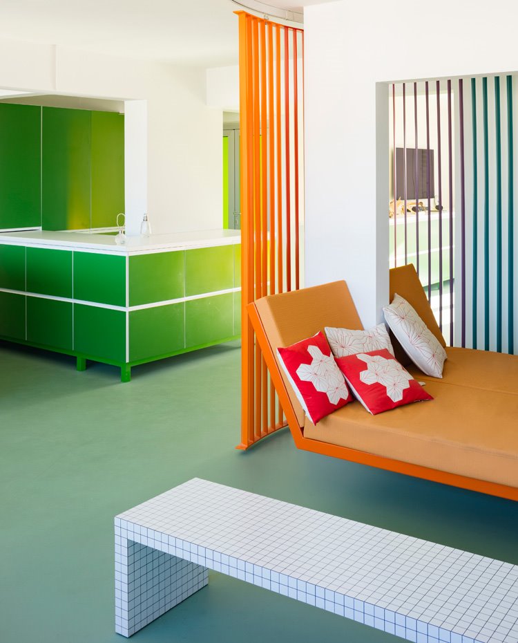 Mesa auxiliar en blanco con filetes en negro, bancada en naranja con cojines en rojo, muebles en verde con sobre blanco