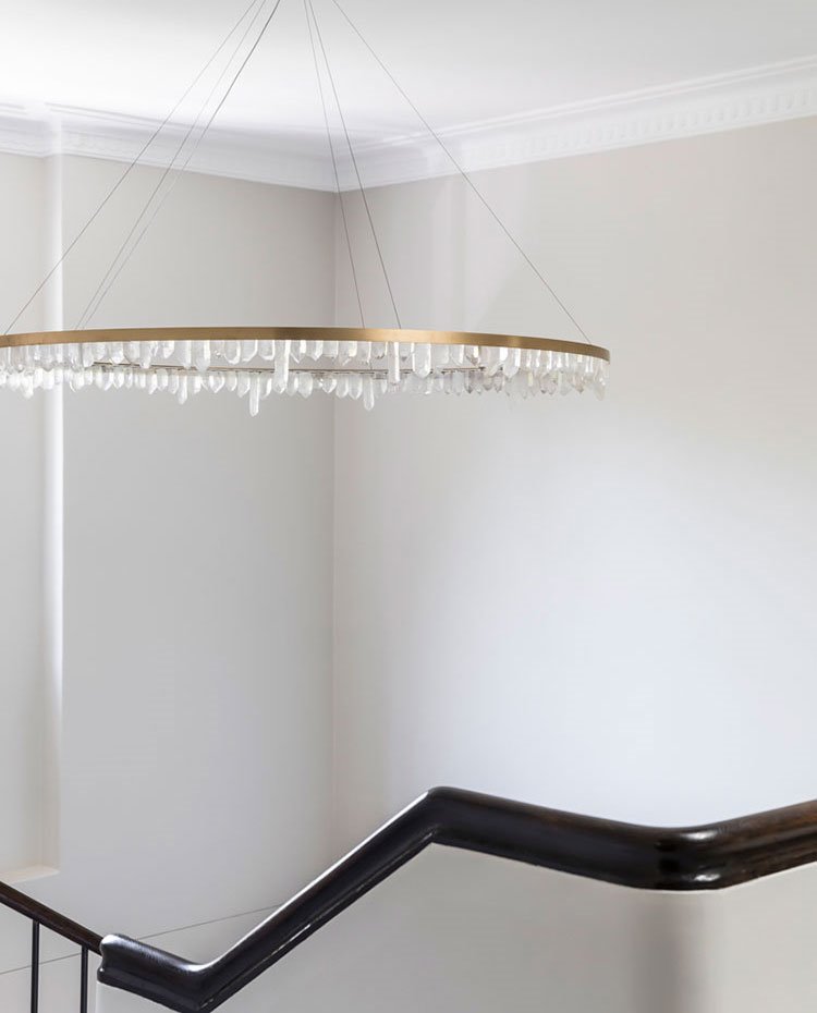 Detalle escalera con pasamanos en madera oscura y luminaria suspendida circurlar en hueco de escalera
