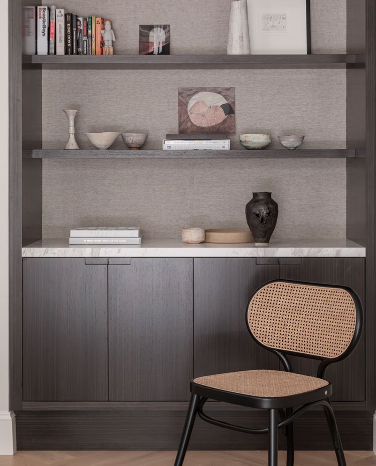 Estantería personalizada con armarios inferior y baldas superiores con fondo forrado en marrón claro. silla de diseño vintage, encimera de módulo en mármol blanco
