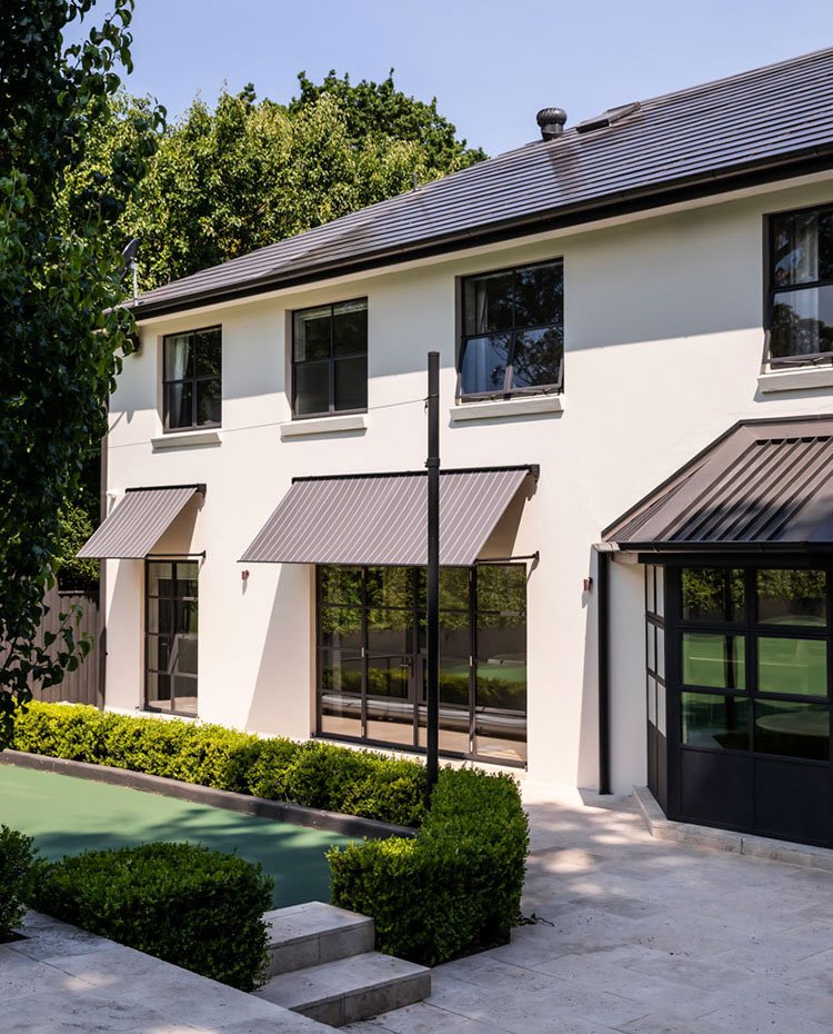 Exterior vivienda con toldos marrones, fachada en blanco y zona ajardinada