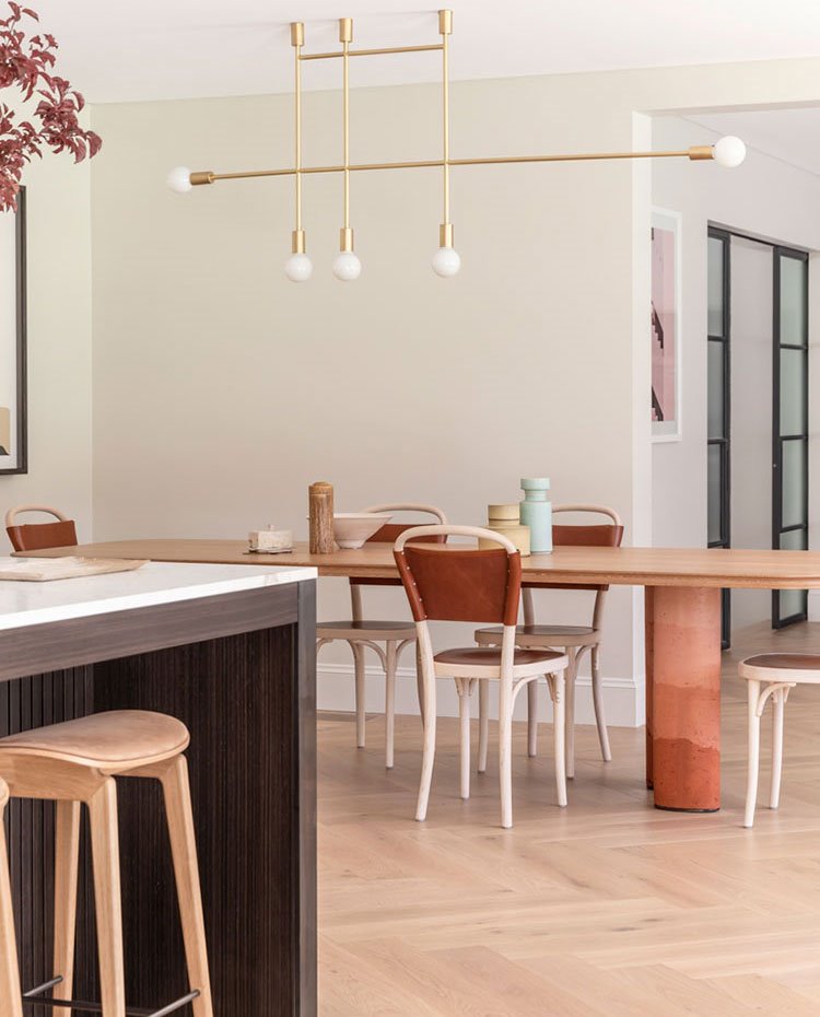 Mesa de comedor junto a cocina, con isla de trabajo y taburetes de madera clara