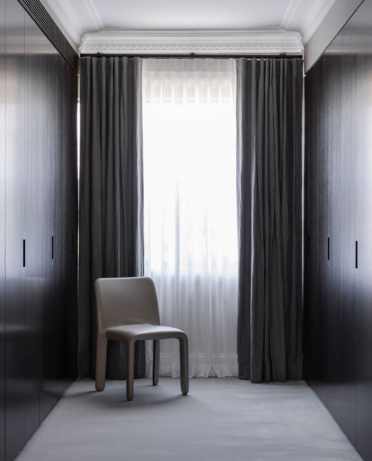 Vestidor revestido de armarios con tiradores integrados, cortinas en gris, silla tapizada de piel color gris, suelo emmoquetado
