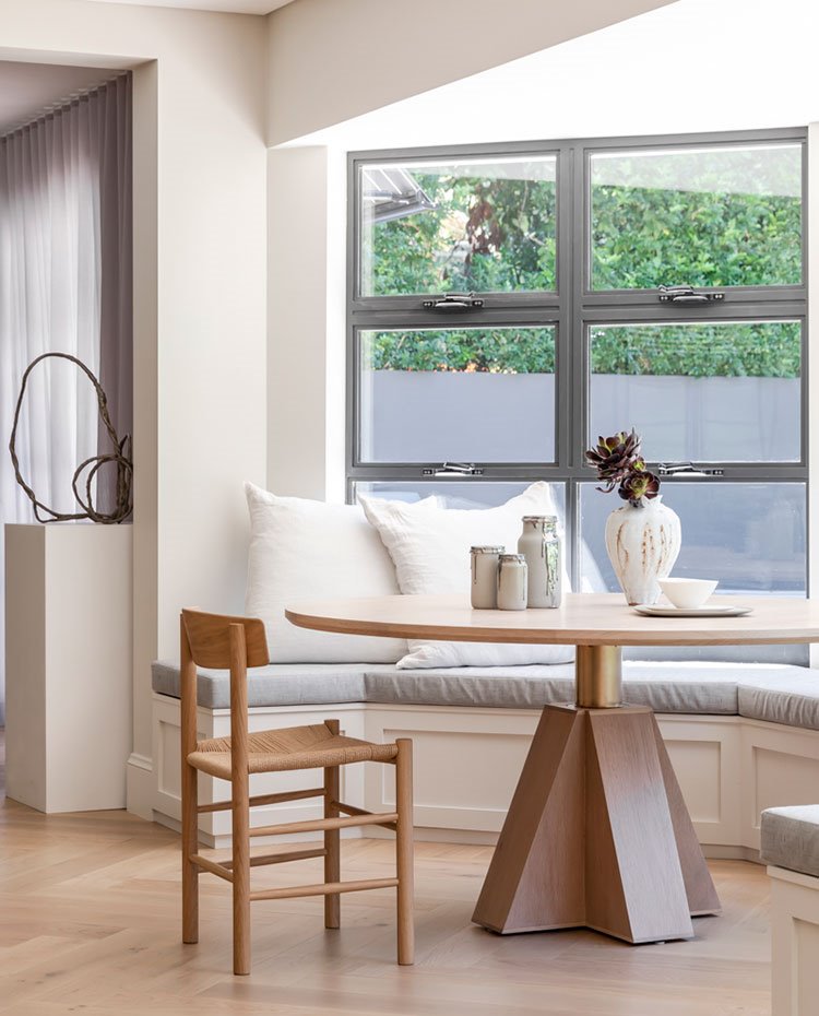 Zona de comedor junto a exterior con cerramiento acristalado y bancada dispuesta en el extremo dispuesta en semicírculo, con mesa de comedor circular y silla en madera