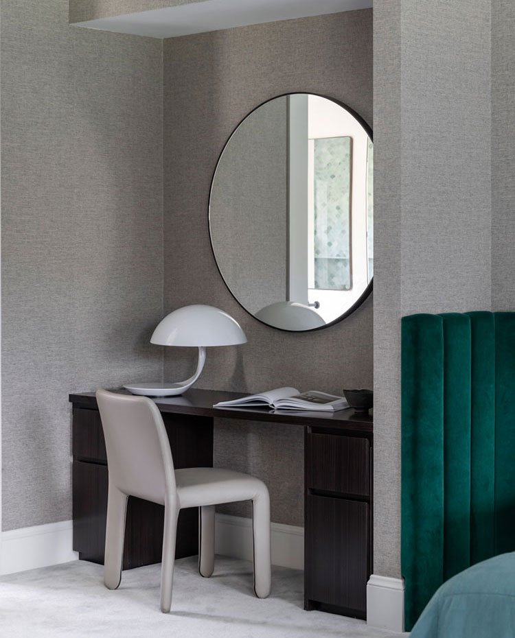 Zona de trabajo con mesa con cajones hecha a medida en madera oscura, silla de piel gris, luminaria de sobremesa con pantalla de cirsta y espejo redondo