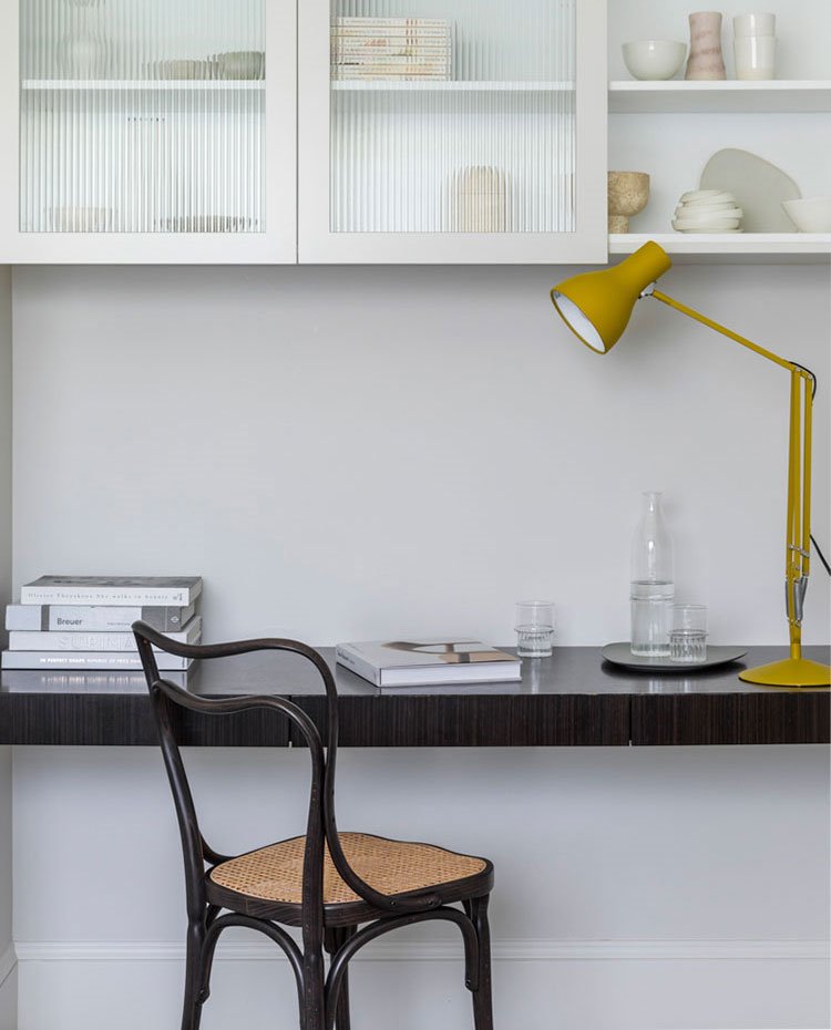 Zona de trabajo con silla vintage, mesa de trabajo hecha a medida, luminaria de sobremesa amarilla, armario superior en blanco con frentes de cristal esmerilado