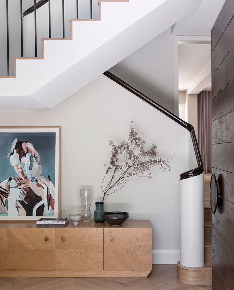 Zona de vestíbulo con mueble bajo de madera y suelo en zig-zag de madera, escaleras con peldaños en madera clara y pasamanos de madera oscura