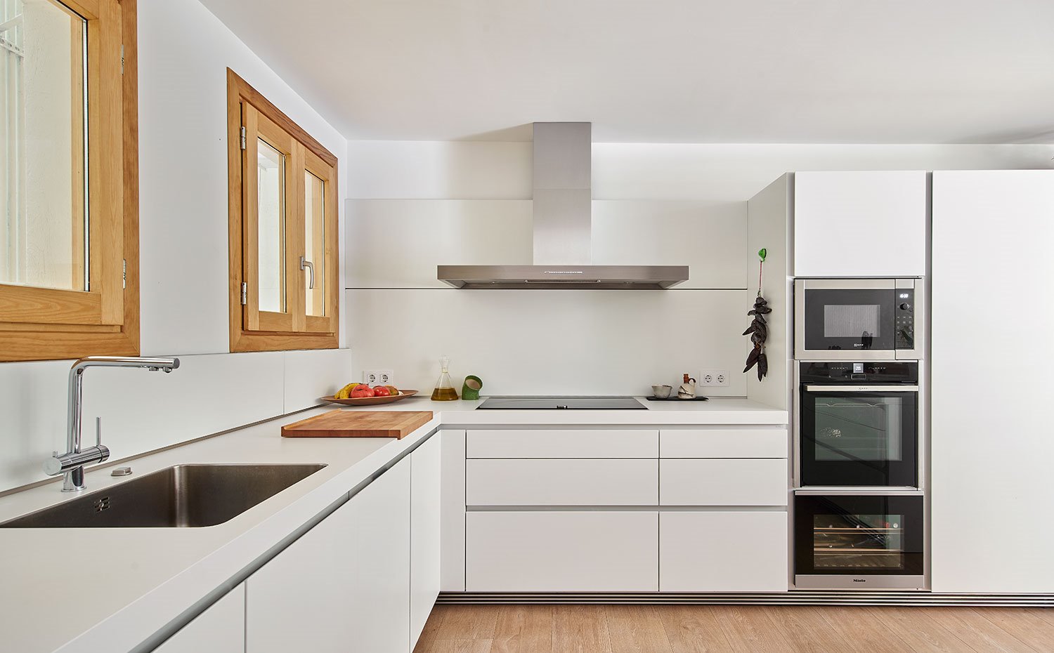 Cocina con mobiliario en blanco con tiradores integrados con perfilería de acero, encimera en blanco