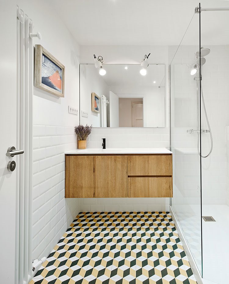Cuarto de baño con suelo con motivos geométricos, mueble bajo lavamanos en madera suspendido, hoja de cristal fija en ducha
