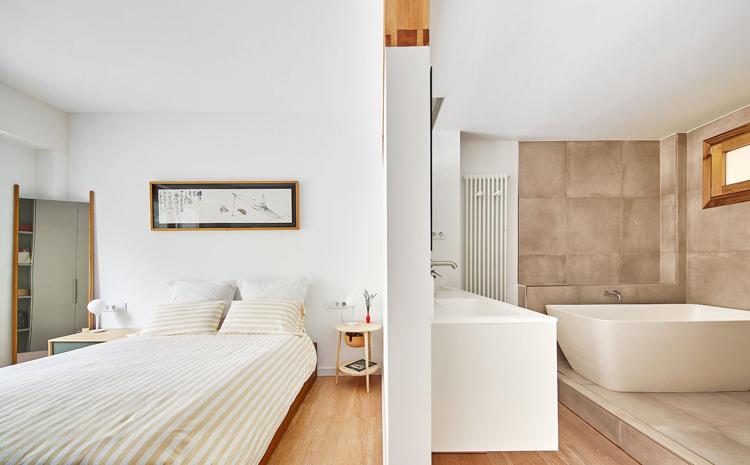 Dormitorio con tabique divisorio con cuarto de baño provisto de bañera exenta sobre revestimiento en color piedra