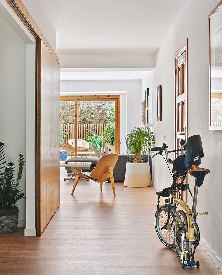 Zona de paso a salón y terraza con puerta corredera, bici plegable y butaca de madera