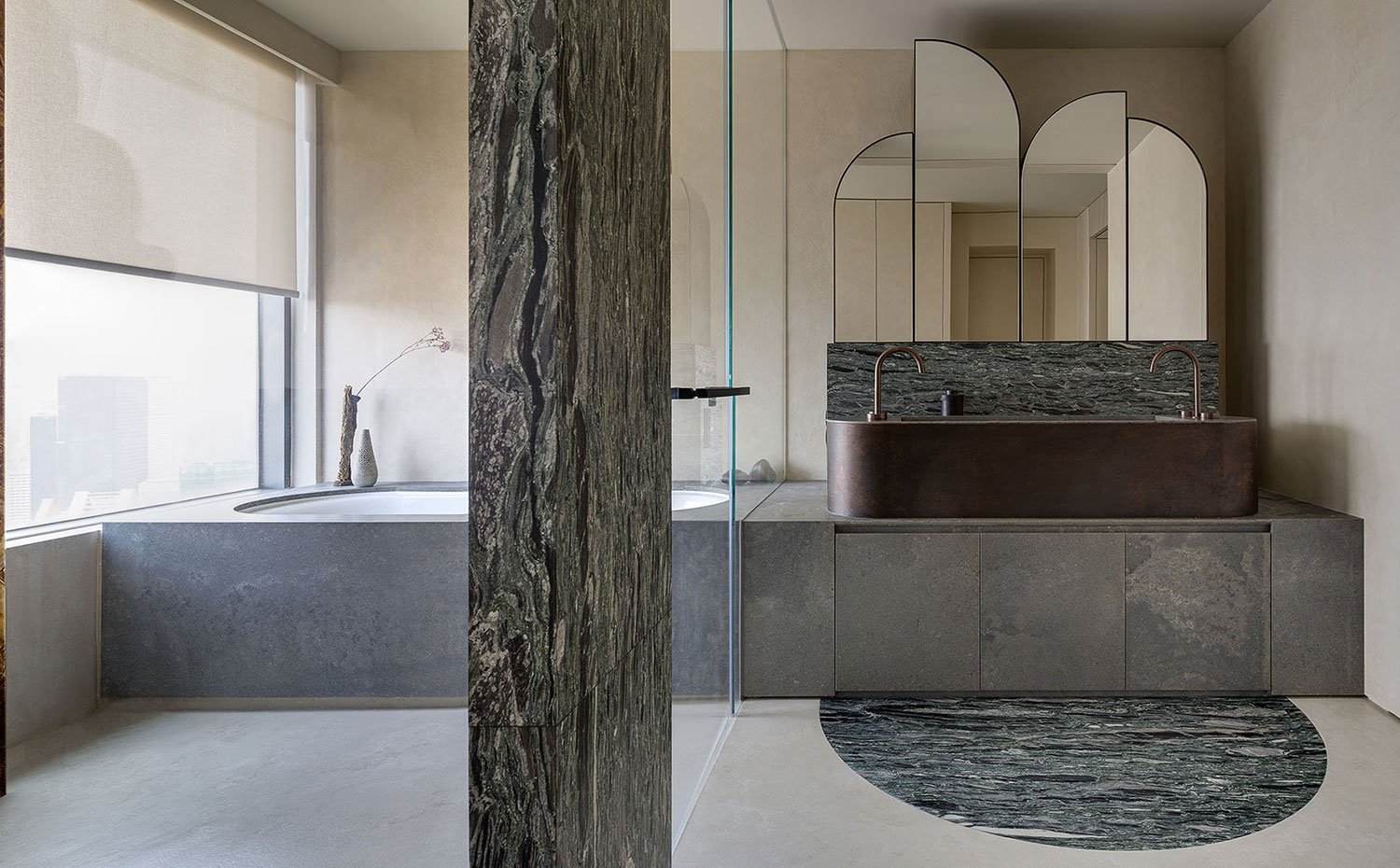 Cuarto de baño con suelo y revestimientos de piedra, bauñera integrada, estor en ventana, cerramiento de cristal