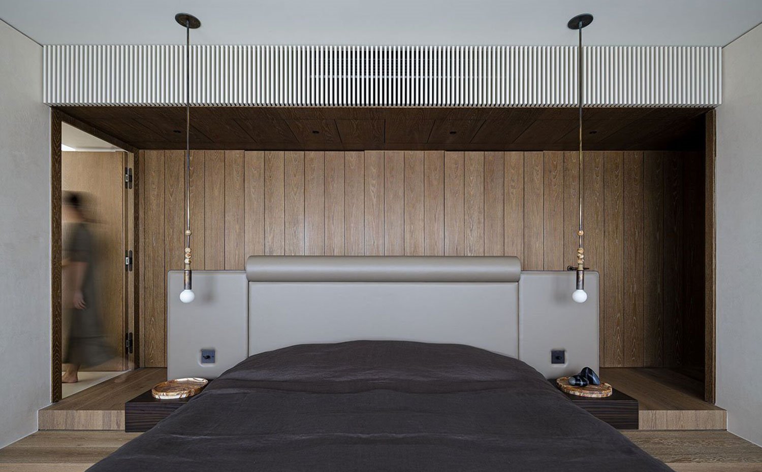 Dormitorio con suelo y revestimiento frontal de madera alistonado, cabezal tapizado en piel, luminarias suspendidas del techo
