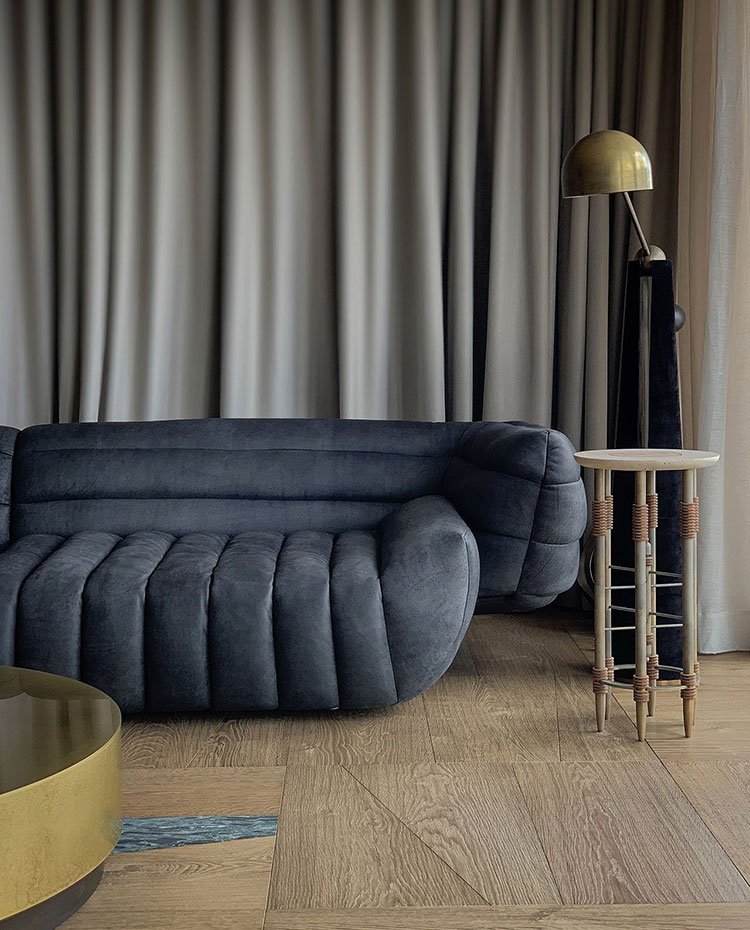 Sofá acolchado en gris, suelo de madera, mesa con sobre en acabado lacado, mesita auxiliar ciruclar