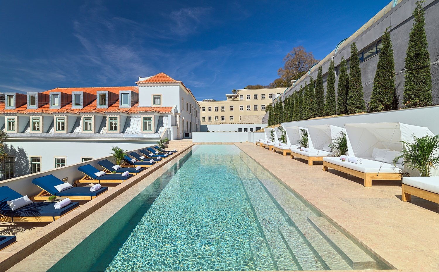 Vistas de la piscina de forma alargada con tumbonas azules y hamacas blancas en lo alto del edificio del hotel