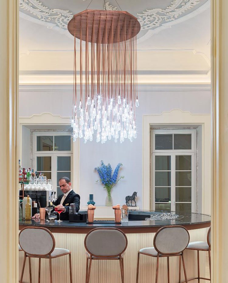 Zona bar con barra circular y taburetes en madera y tapizados en gris, luminaria suspendida con bombillas en forma de lágrima. molduras sobre ventanales