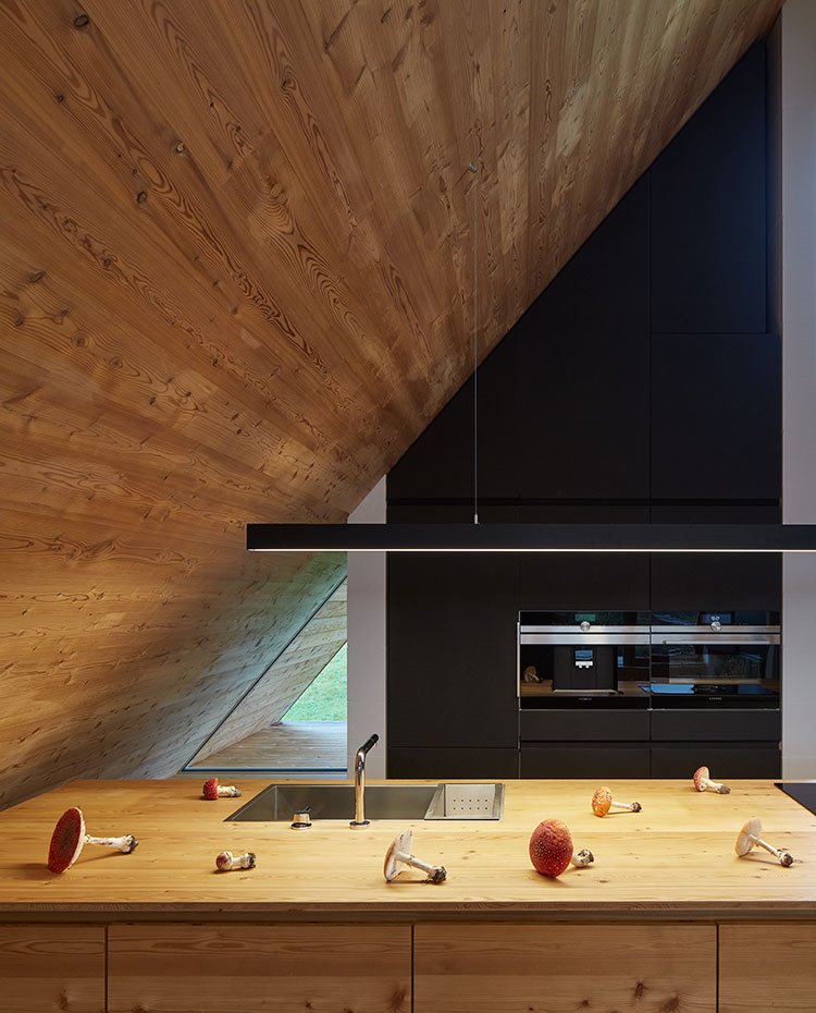 Cocina abierta equipada con isla de trabajo revestida de madera natural, fregadero integrado de acero y armarios de almacenaje en negro