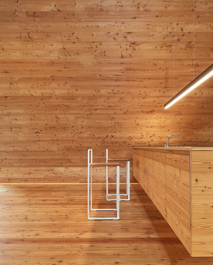 Taburetes de cocina con estructura en madera y asientos del mismo tono que el mobiliario de la cocina y el revestimiento de la sala