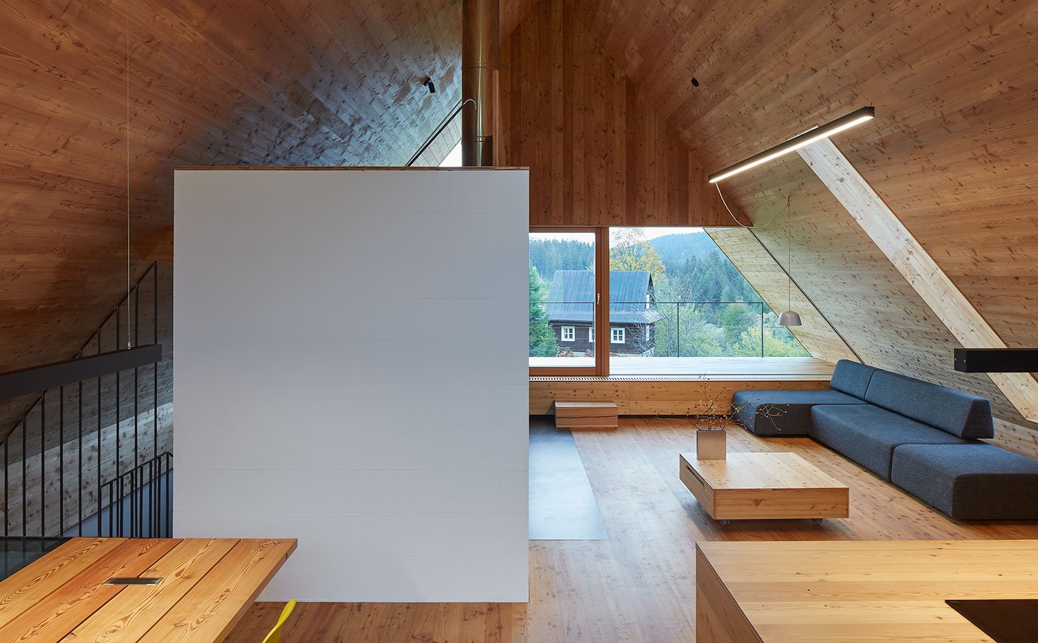 Zona de comedor junto a cocina y salón, con sofá modular en gris oscuro y mesa de centro en madera, a juego con el parquet del suelo