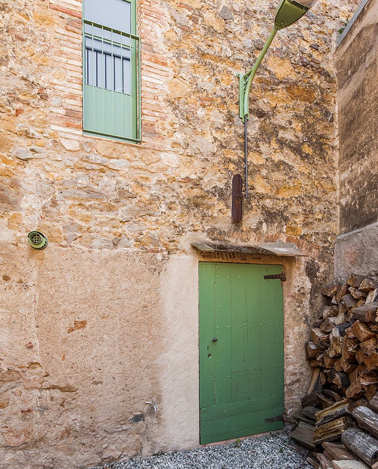 Fachada de piedra con cerramientos y luminaria en verde