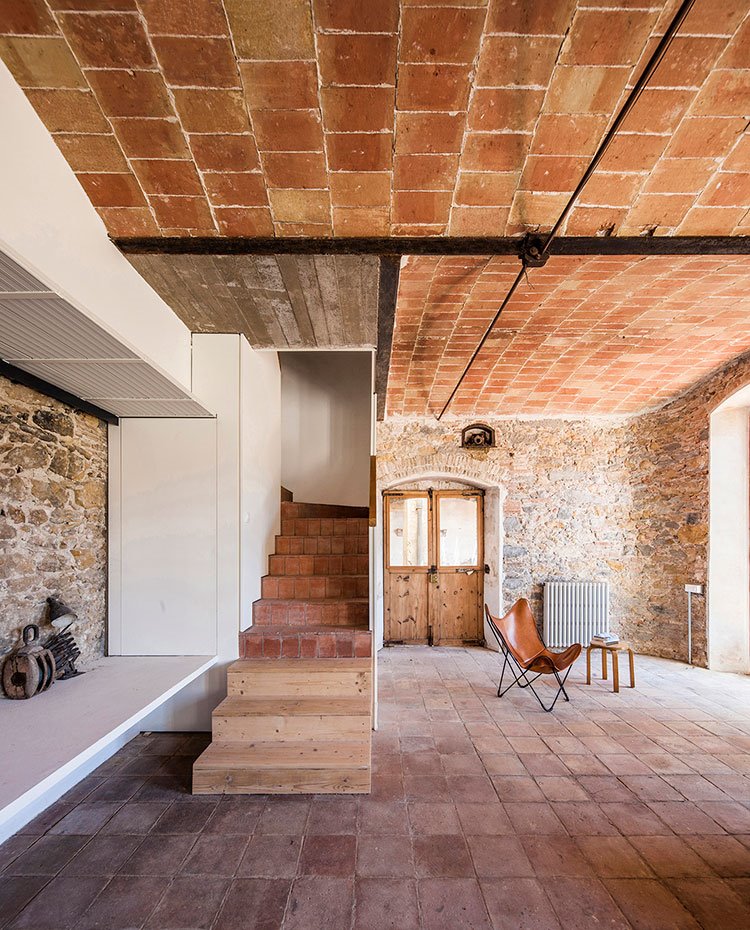 Interior de vivienda con techo en volta catalana, escaleras de madera y gres, asiento en piel y mesita en madera