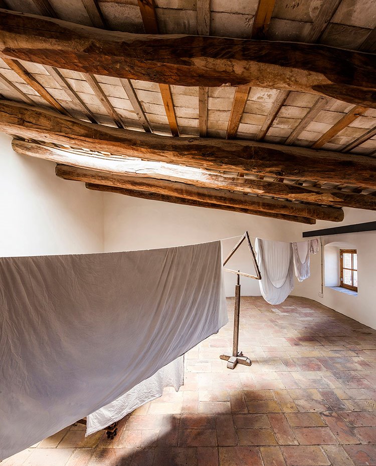 Sala diáfana con cubiertas de madera a modo de buhardilla, con lucernario superior, sábanas tendidas