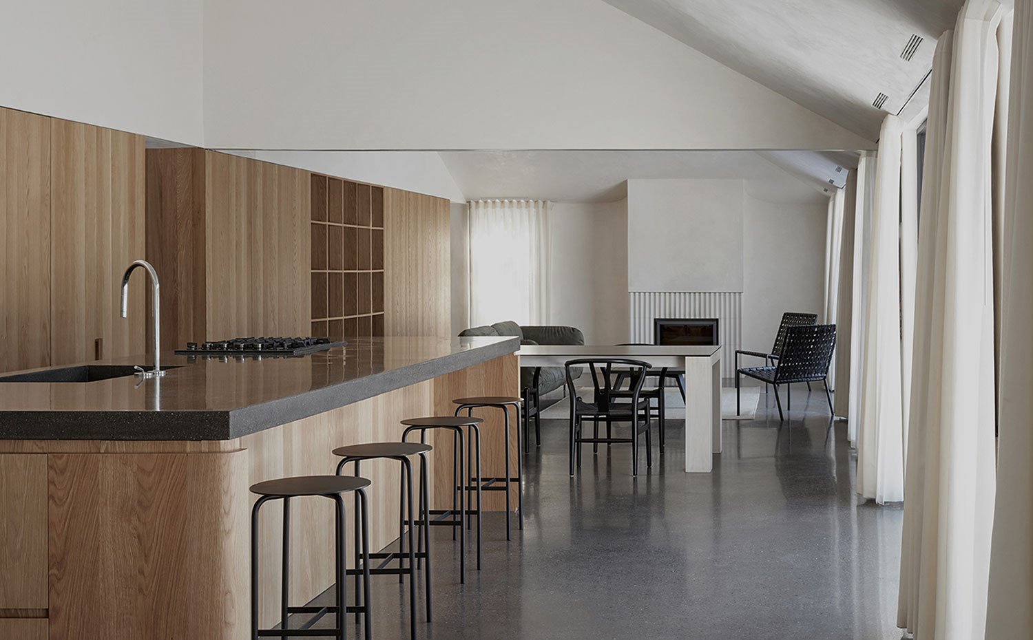 Espacio diáfano con cocina abierta, comedor y salón al fondo con taburetes, sillas y butacas en negro