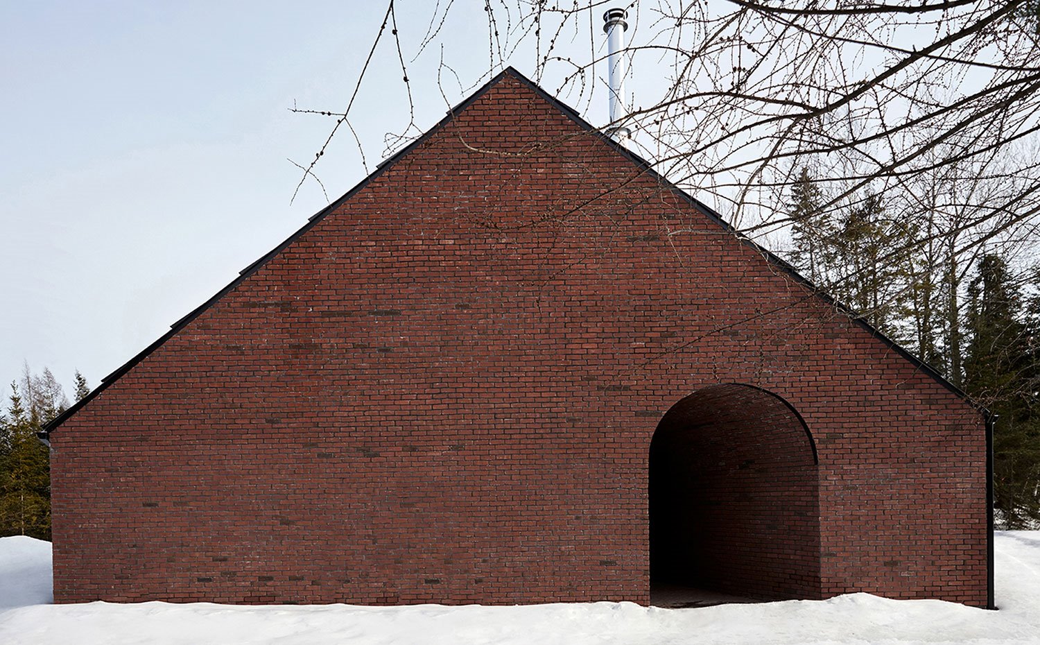 Exterior compacto de la vivienda con fachada en ladrillo visto y entorno natural nevado