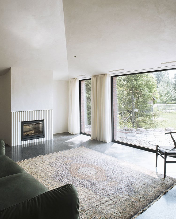 Salón con chimenea integrada con frente alistonado, alfombra sobre revestimiento pulido, sofá verde y cerramiento acristalado