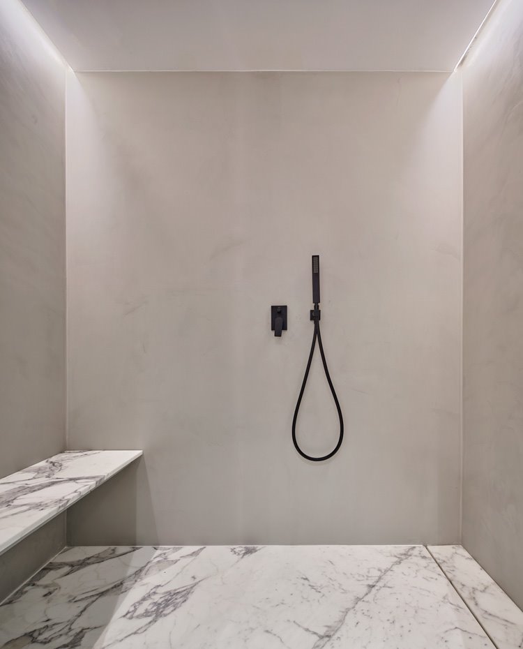 Amplia ducha con grifería acabada en negro y asiento de obra y plato de ducha en marmol