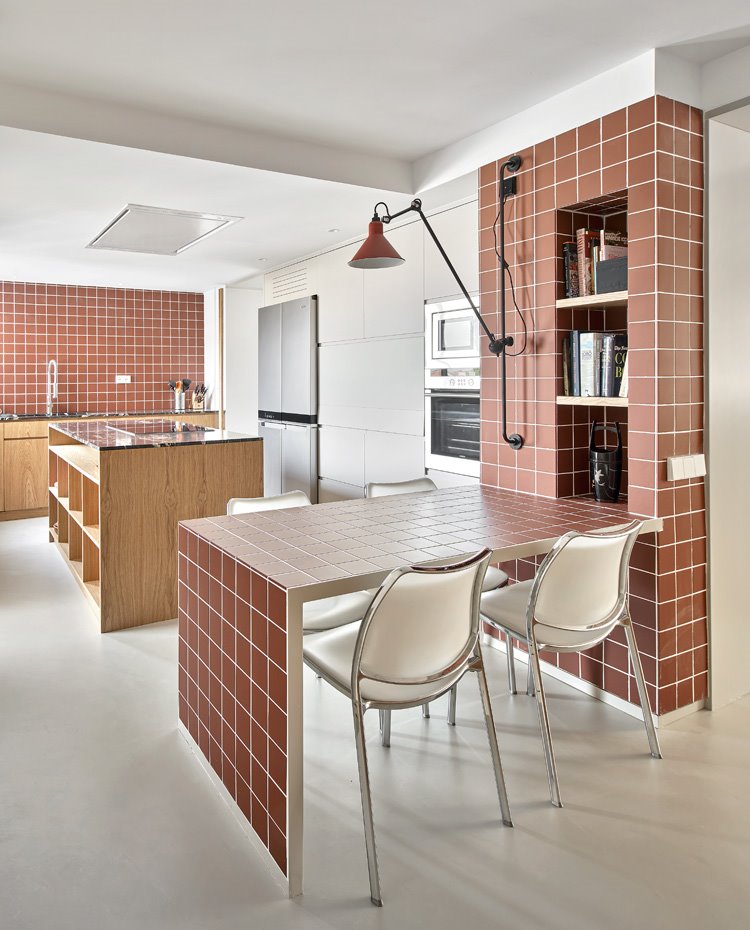 Cocina con mesa de office hecha de obra, sillas en blanco e isla de trabajo central con estantes abiertos