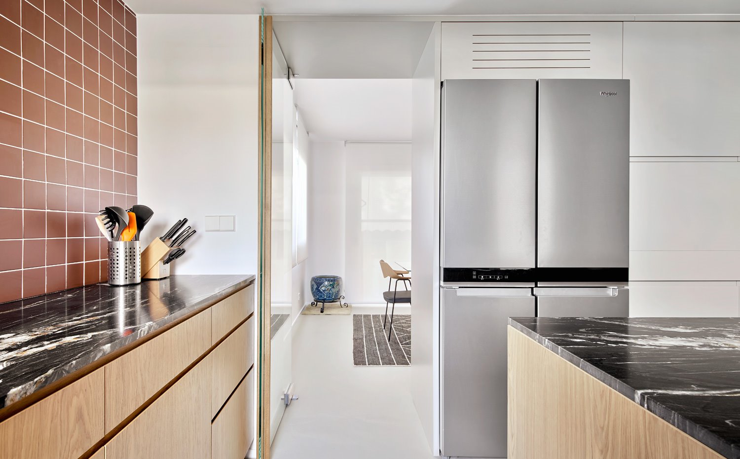 Cocina con módulos de madera, encimeras de mármol negro, eletrodomésticos en acero inoxidalbe, pared revestida de baldosas cerámicas