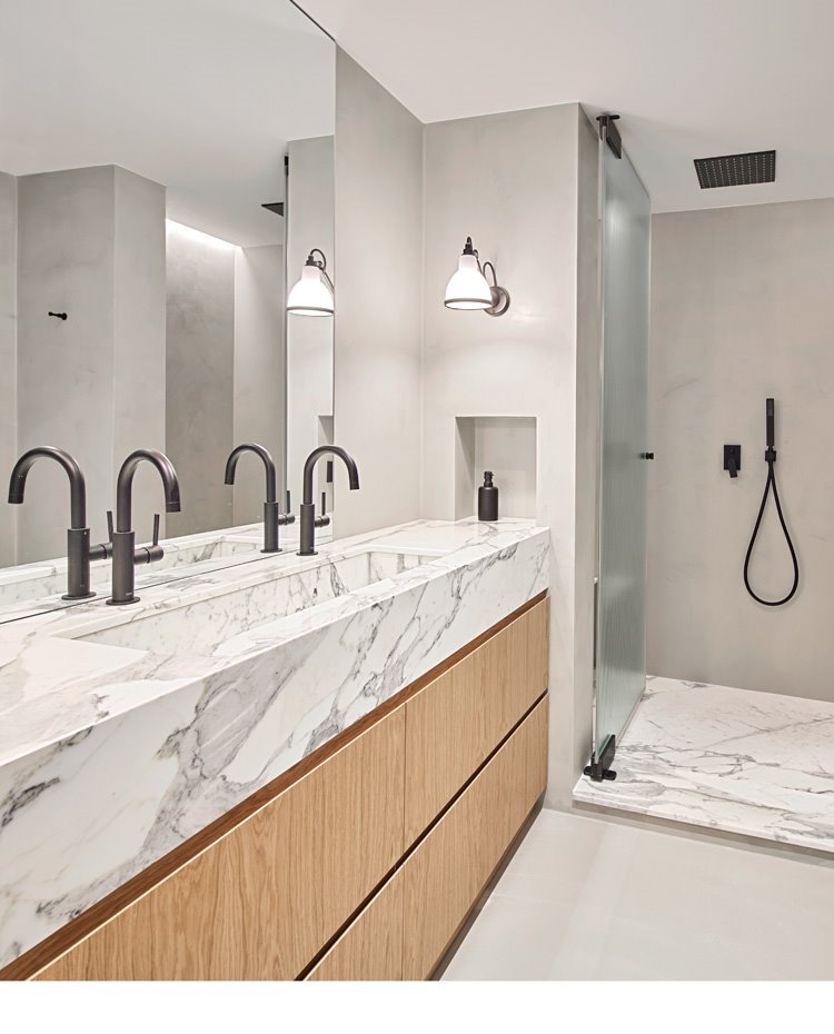 Cuarto de baño con plato de ducha y encimera en mármol blanco, grifería acabada en negro, módulos en madera natural