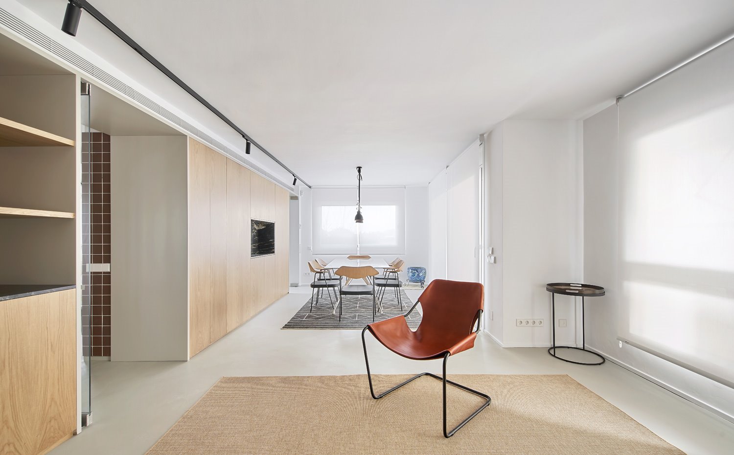 Salón y comedor abiertos en una amplia sala, silla de piel marrón sobro alfombra beige y al fondo, mesa de comedor de cristal