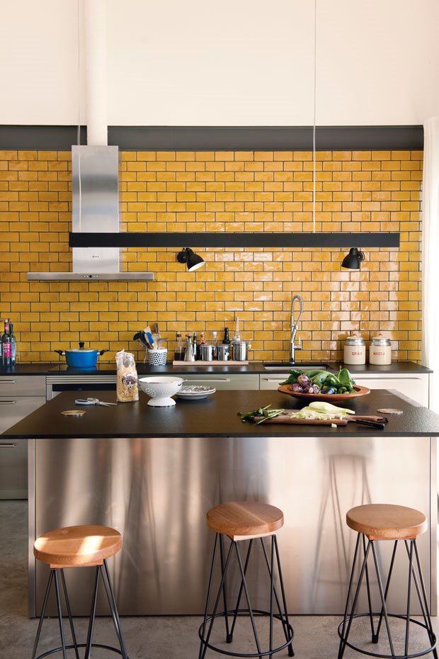 Cocina amarilla con encimera de granito negro y taburetes