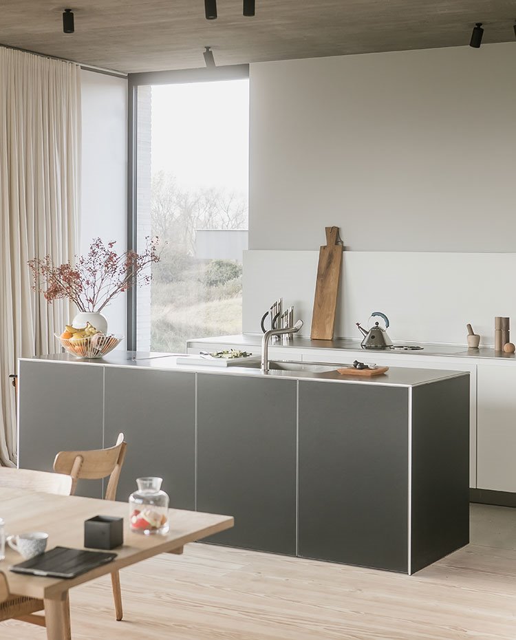 Cocina con isla en negro, mesa y sillas de madera, cortinas en crudo, frente de armarios bajos blancos
