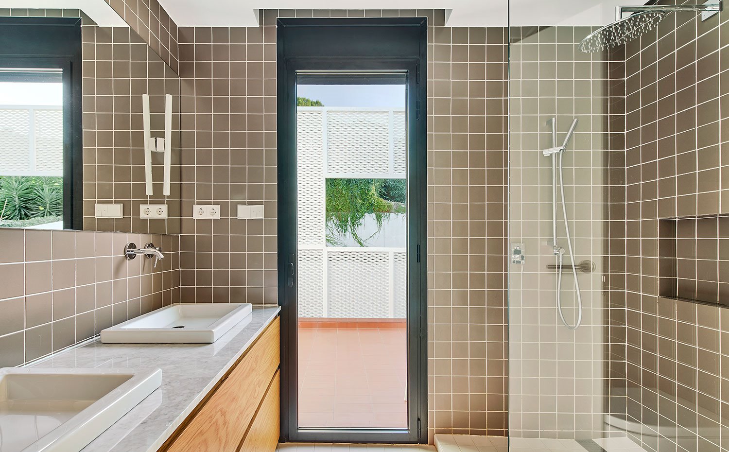 Cuarto de baño con encimera de mármol, mueble de madera y revestimiento en baldosas marrones de pequeño formato
