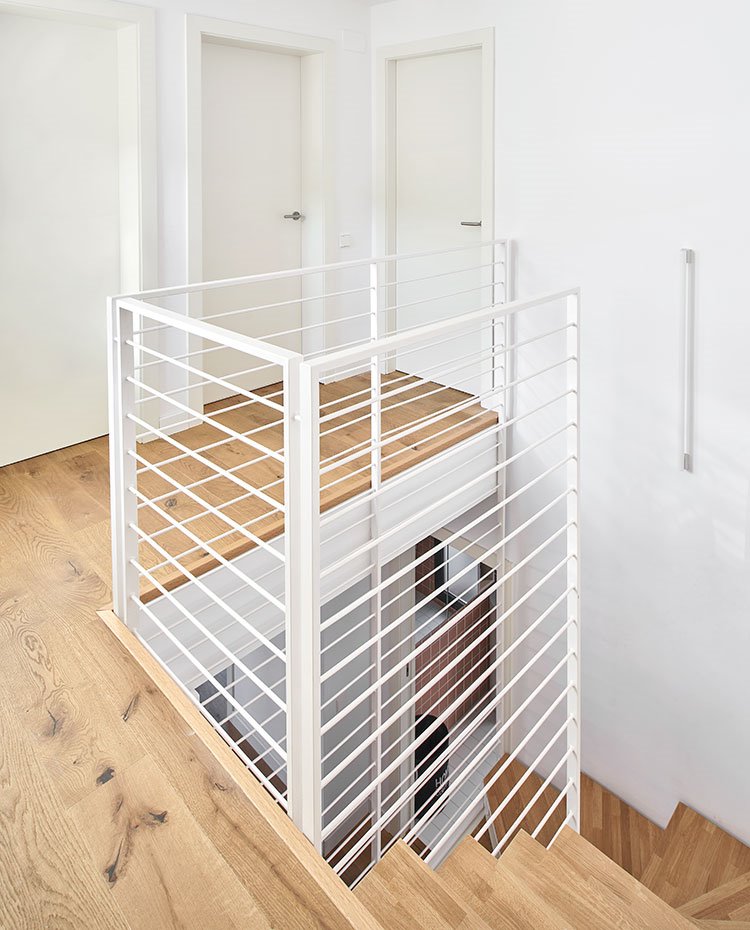Peldaños y suelo de madera frente a puertas, estructura de escalera y paredes en blanco