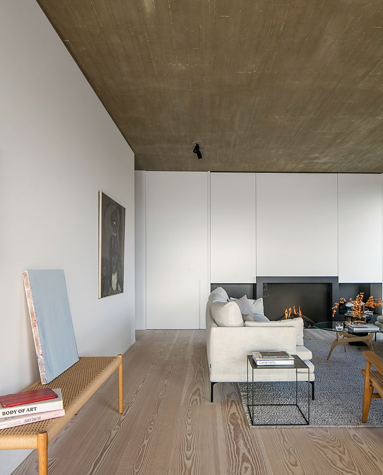Salón con bancada de fibras y madera, suelo de madera, sofá gris claro, alfombra gris, pared panelada, chimenea integrada