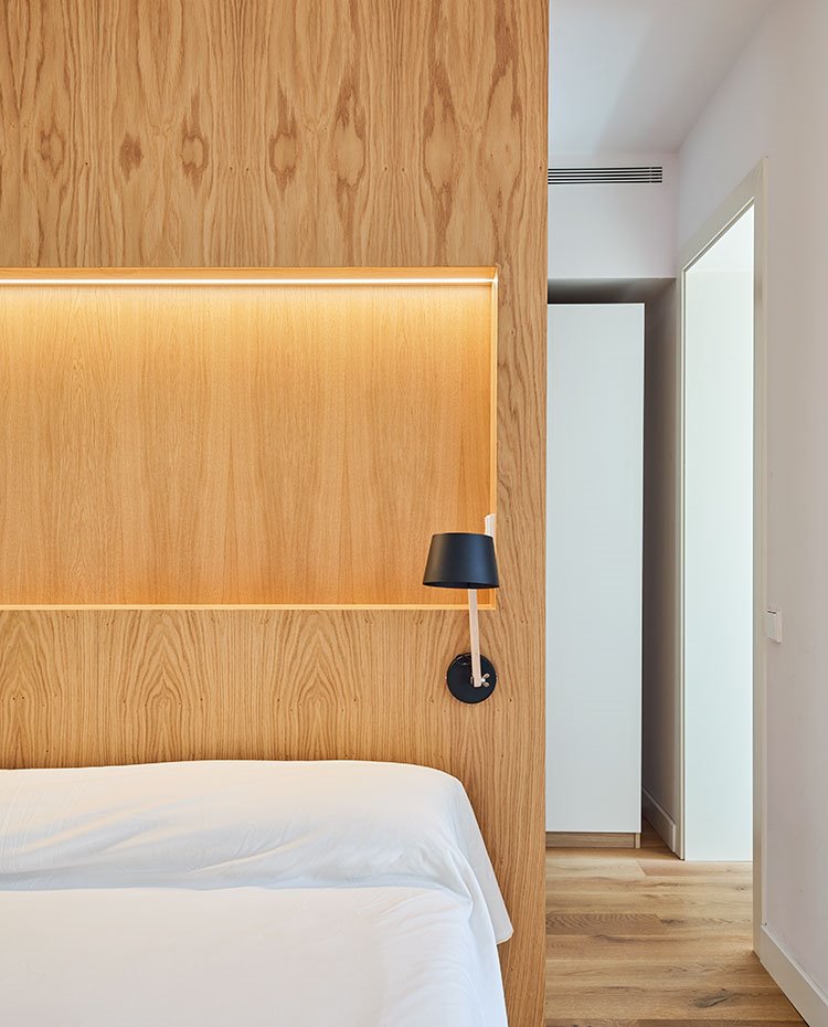 Zona de paso hacia vestidor y cuarto de baño con carpintería en acabado madera para el cabecero y blanco para armarios