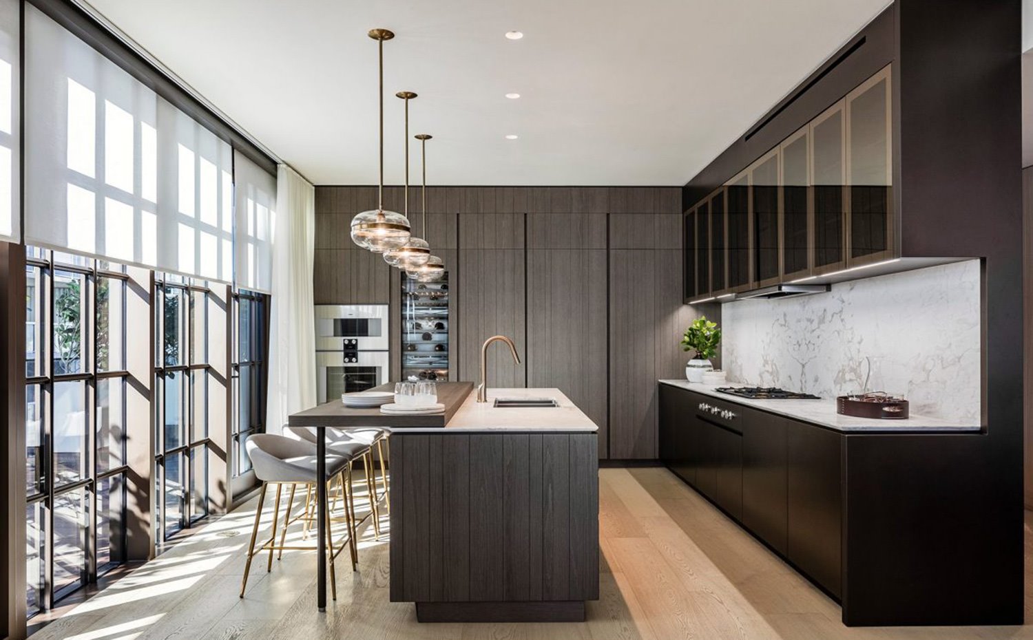 Cocina con isla central, revestimiento en madera oscura, luminarias suspendidas en línea sobre zona de office