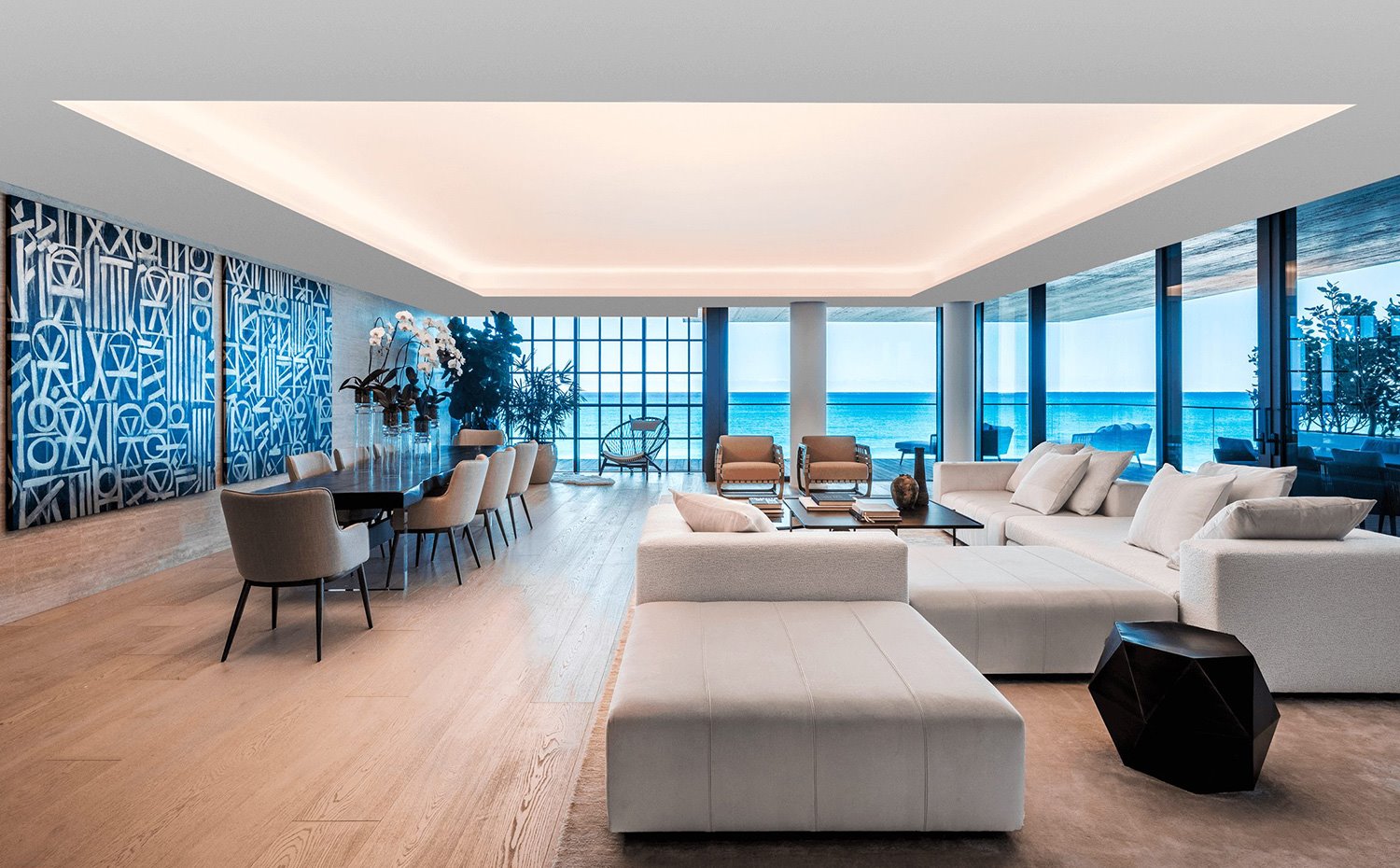 Salón y comedor con amplio sofá modular en blanco, mesa rectangular con sillas tapizadas de pie, suelo de madera