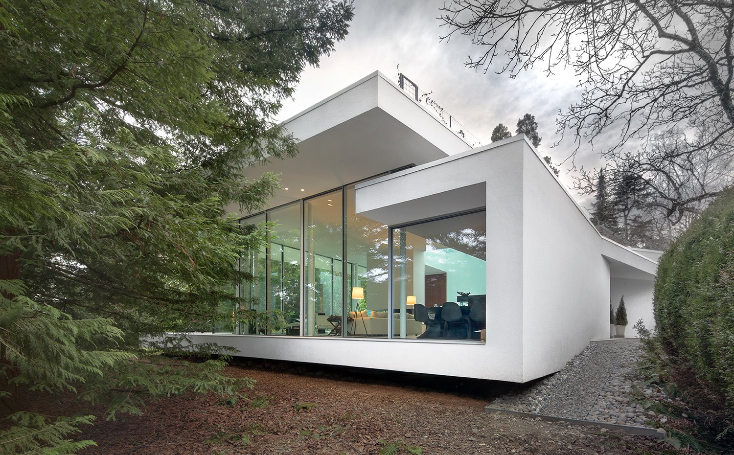 Exterior de la casa con estructura en voladizo sobre desnivel, con fachada en blanco y cerramientos de cristal