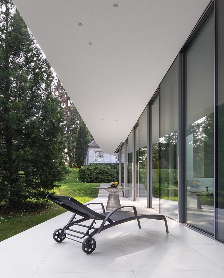 Terraza exterior frente a salón, hamaca y mesa en acabado metalizado, suelo en blanco