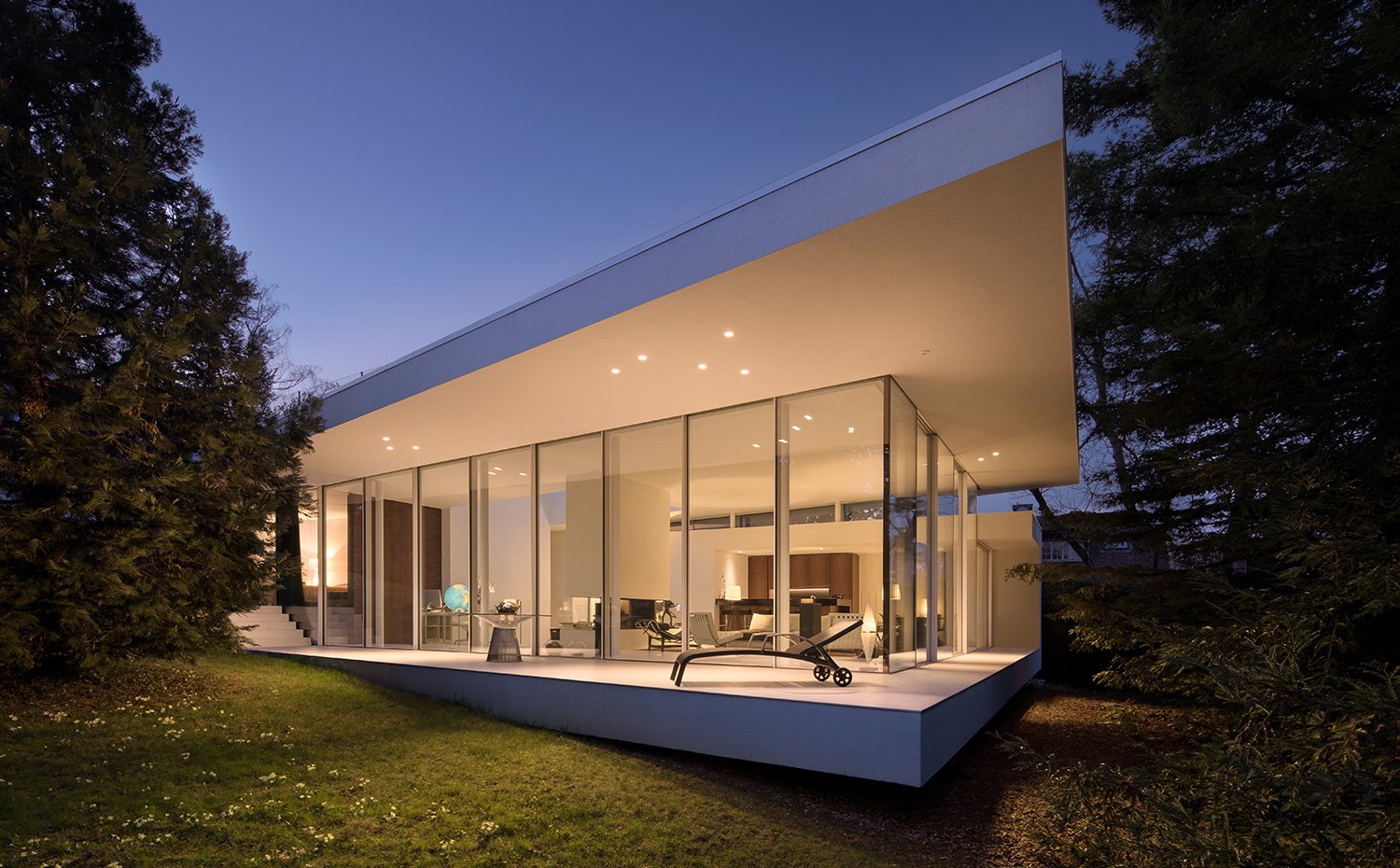 Vista exterior con luces con fachada de cristal, saliente con hamaca y entorno boscoso