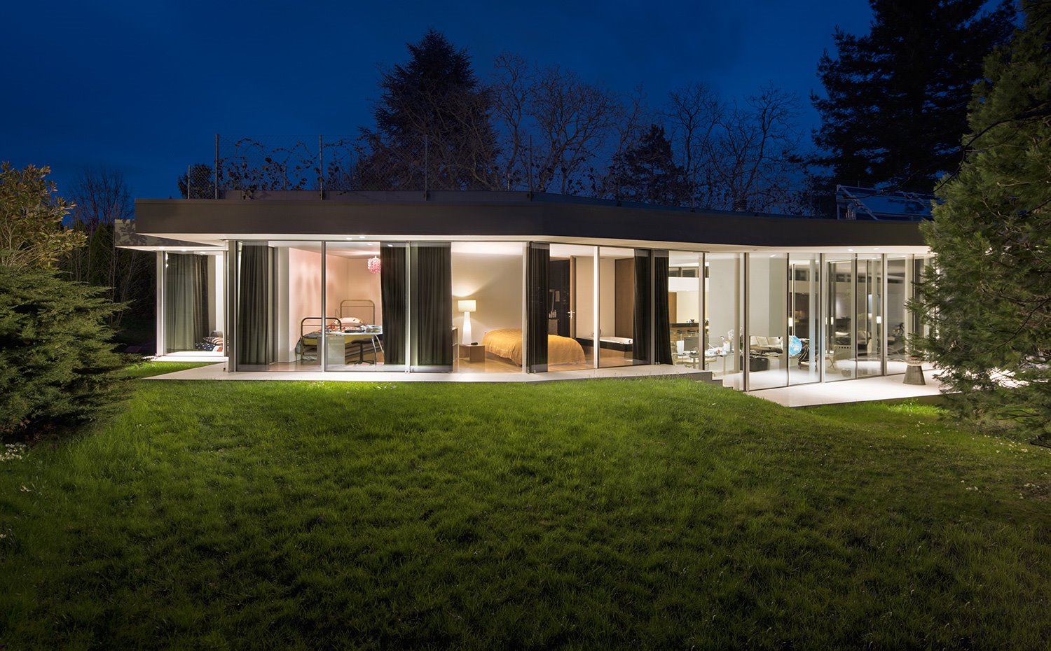 Vista exterior nocturna de la vivienda con zona ajardinada y disposición a una sola planta