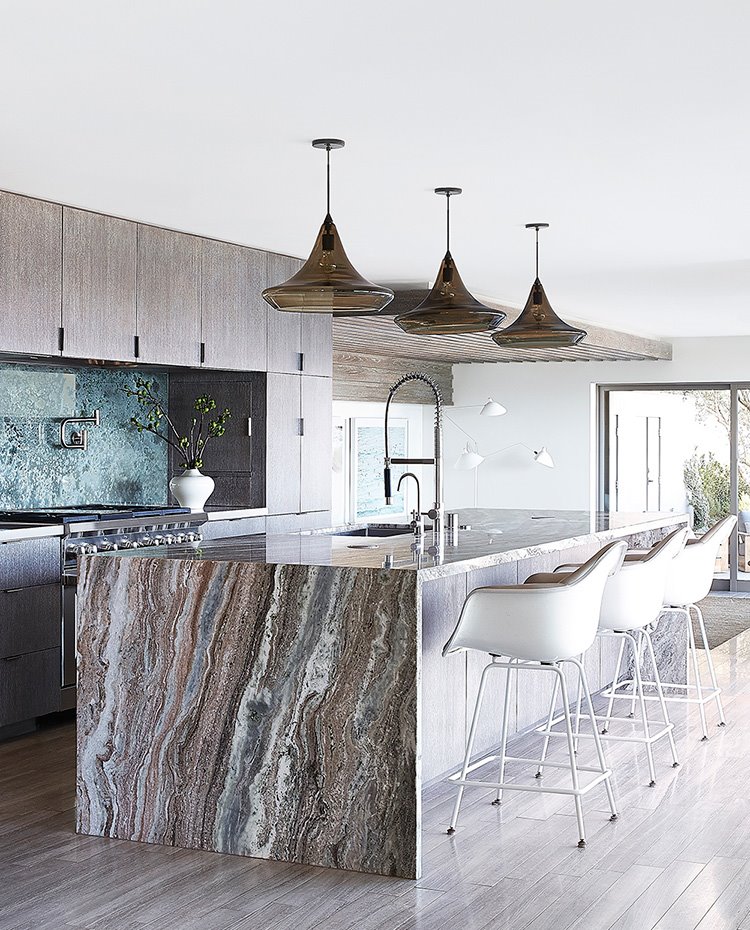 Cocina abierta con taburetes en blanco, luminarias suspendidas con pantalla de cristal, isla de trabajo de mármol, mobiliario de madera