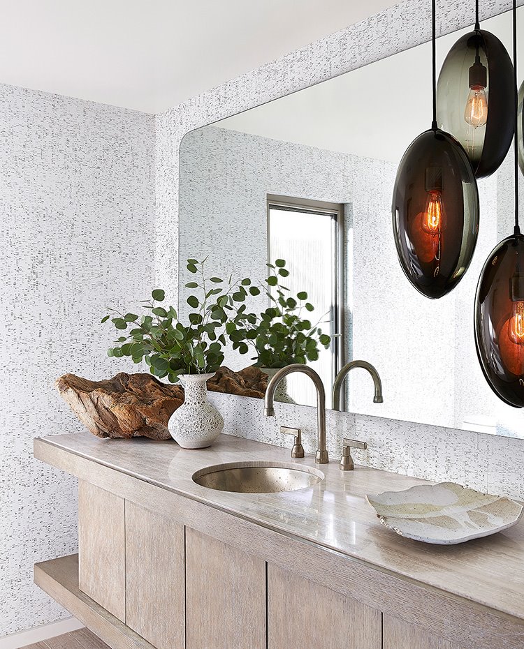 Cuarto de baño con mobiliario en madera, encimera en mármol, revestimiento en papel pintado y espejo rectangular con los cantos curvos