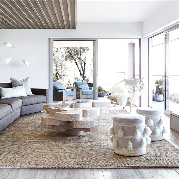 Salón con mobiliario en madera, sofá en marrón, cojines y poufs en crido, alfombra en fibras naturales